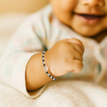 Load image into Gallery viewer, Baby&#39;s hand wearing a black beaded bracelet with a heart charm, blurred background
